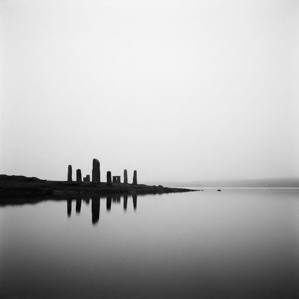 Monolithic ancient structures reflected in still water beneath a vast misty sky